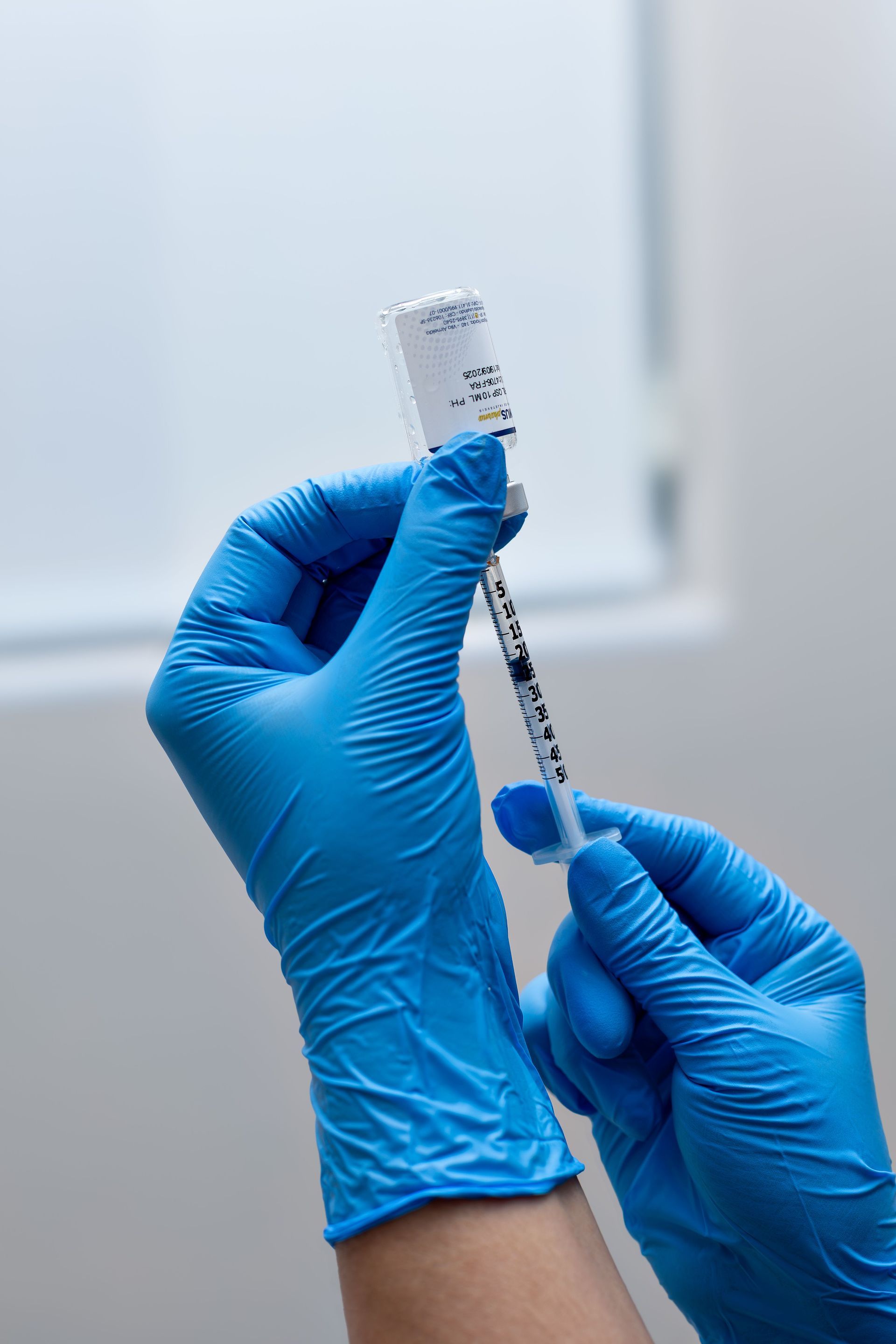 Mains gantées tenant une seringue et un flacon, prélevant un vaccin dans un environnement clinique