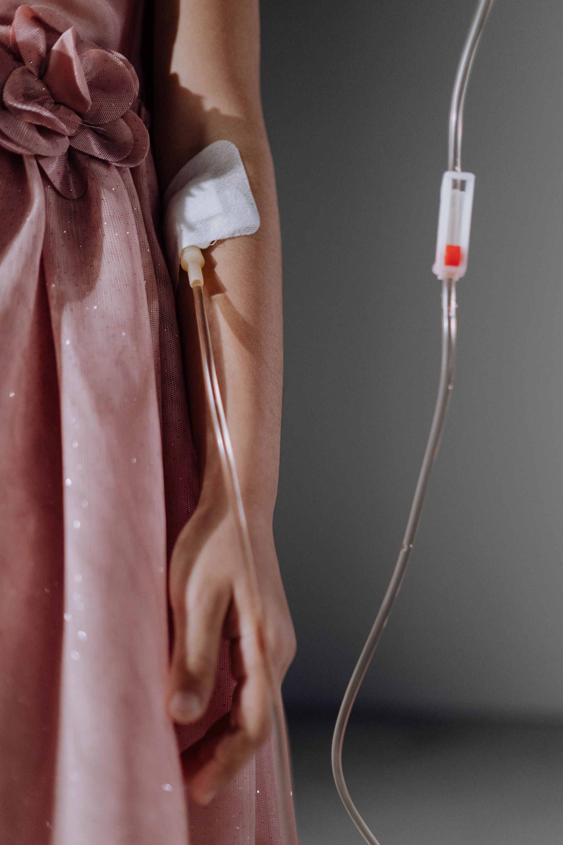 Une perfusion intraveineuse est reliée au bras d'une personne à côté d'une robe en satin rose.