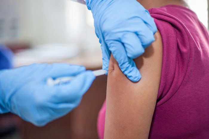 Des mains gantées administrent une injection de vaccin dans le haut du bras d'une personne