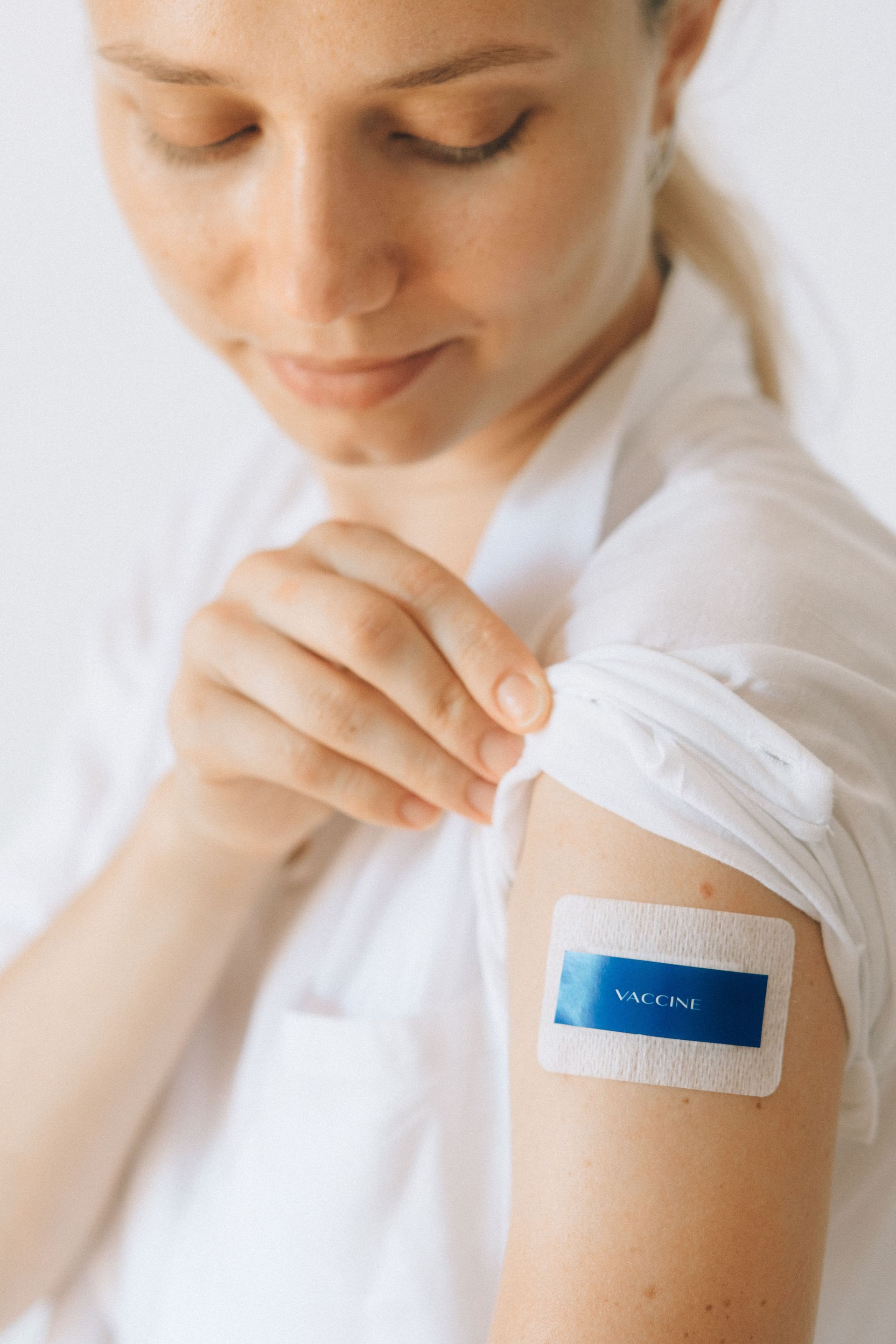 Une personne remonte sa manche pour montrer un bandage au bras avec un patch adhésif bleu.