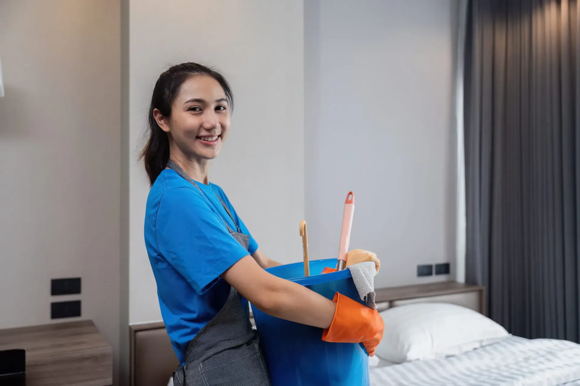 En un dormitorio, una persona sonriente, vestida con una camisa azul y guantes 