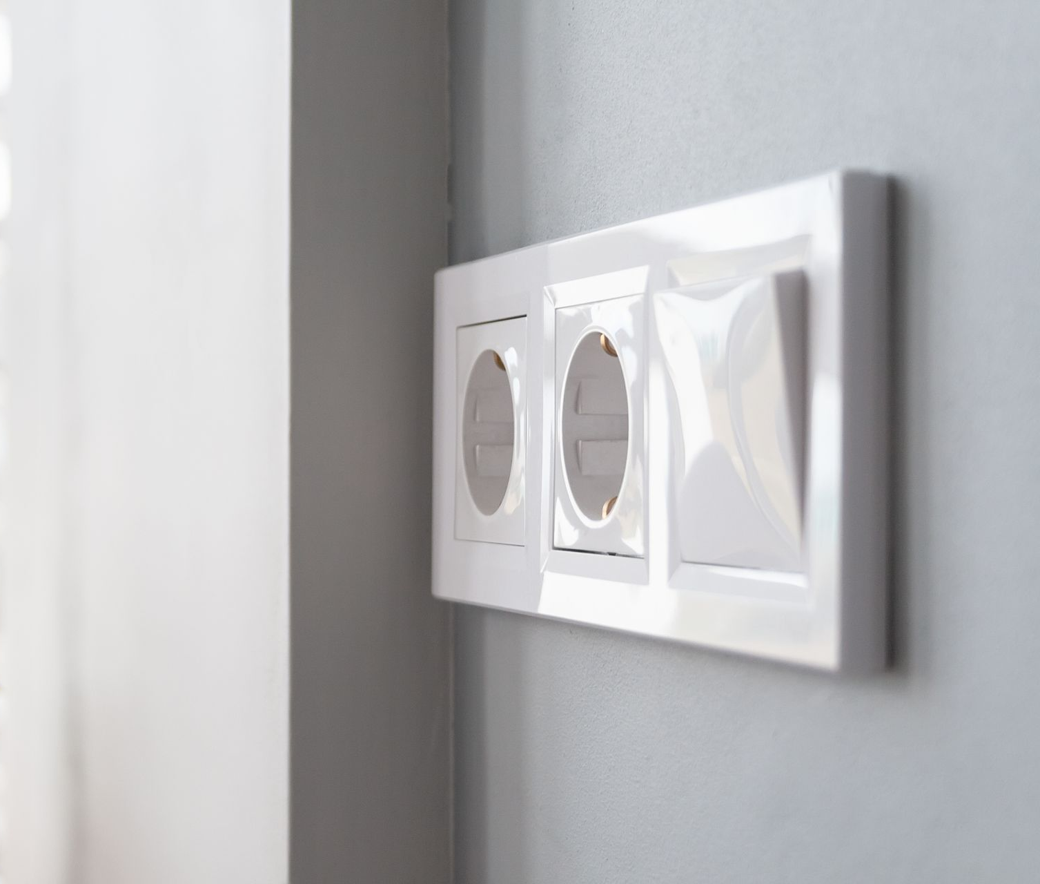 Plaque de prise et d'interrupteur blanche sur un mur gris.