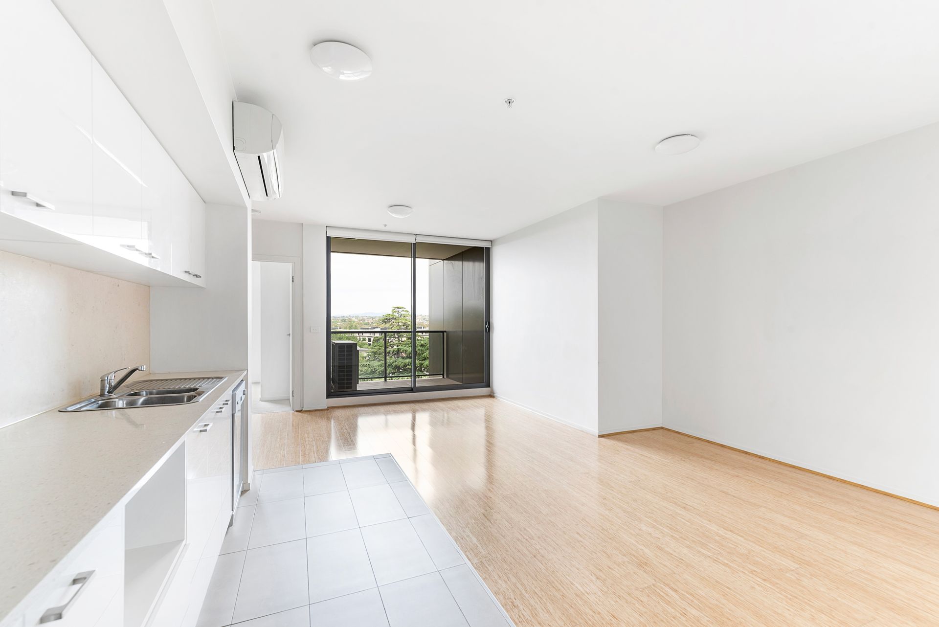Intérieur d'appartement vide et lumineux, avec murs blancs, cuisine, parquet et balcon.