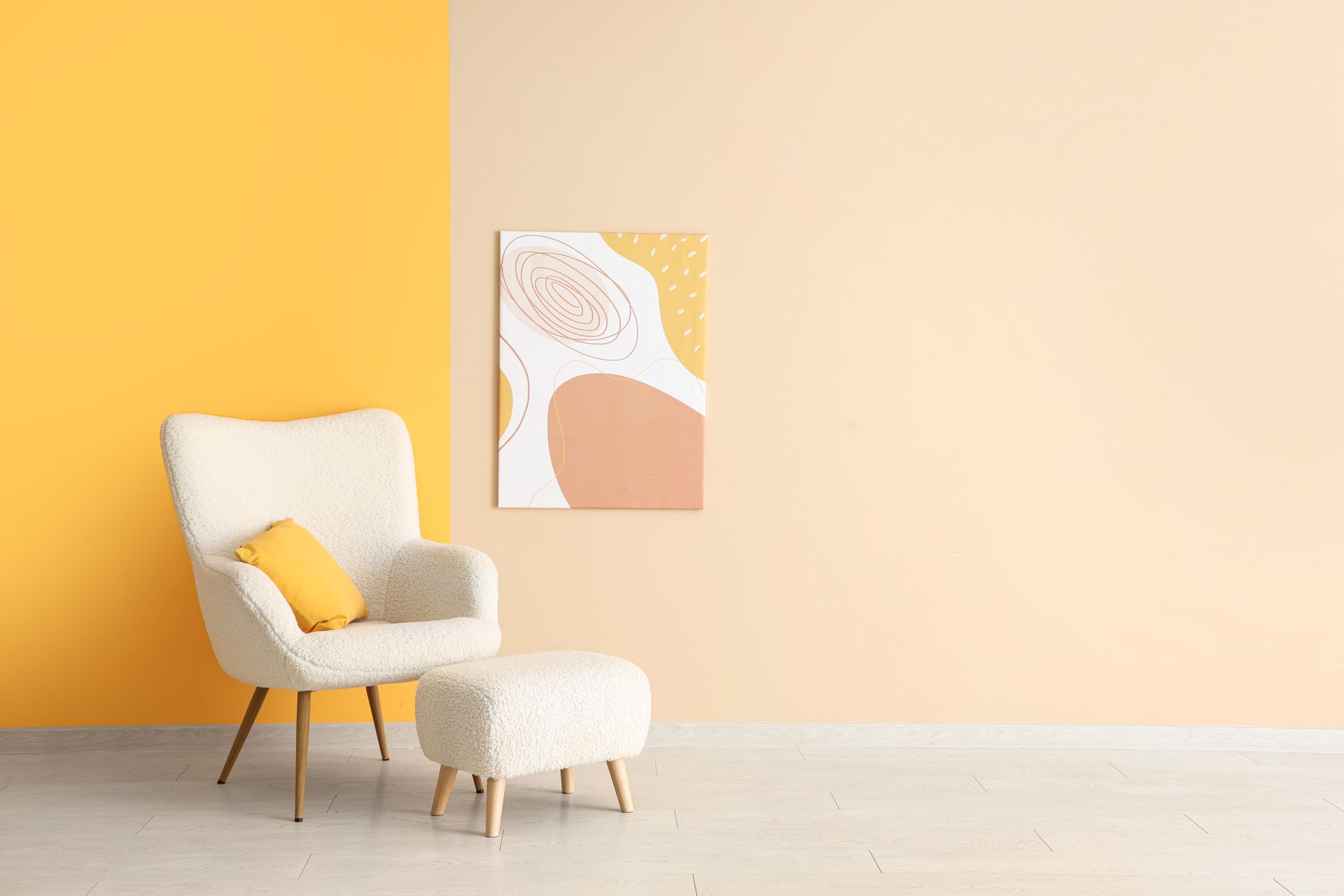 Pièce cosy avec un fauteuil crème, un pouf et un coussin jaune. Tableau abstrait au mur, fond bicolore jaune.