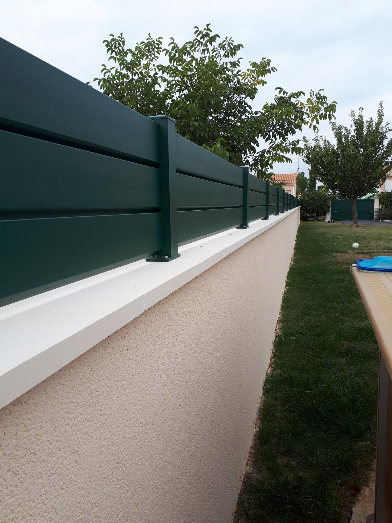 Clôture avec lames horizontales de couleur verte sur un muret 