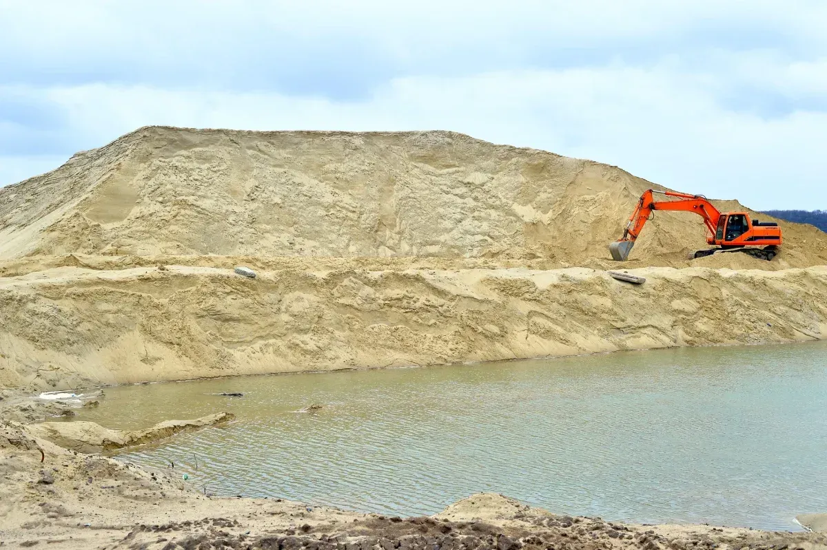 Una excavadora está sentada encima de una pila de tierra al lado de un cuerpo de agua.