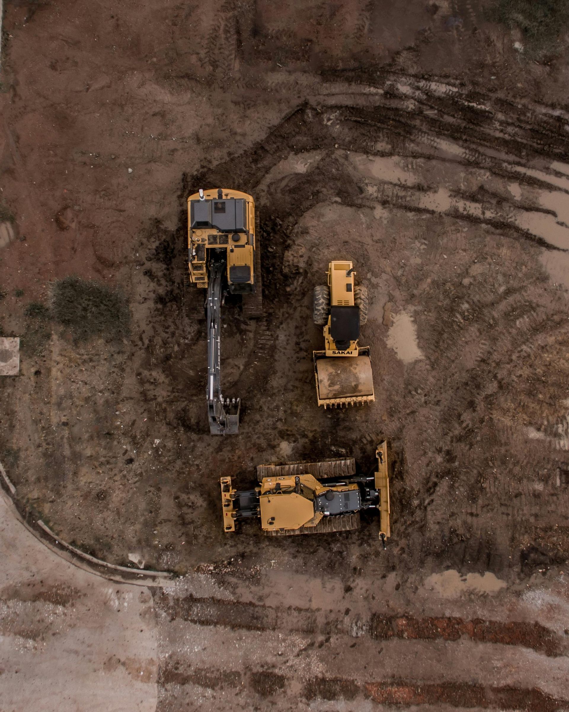 Una vista aérea de tres vehículos de construcción estacionados sobre un campo de tierra.