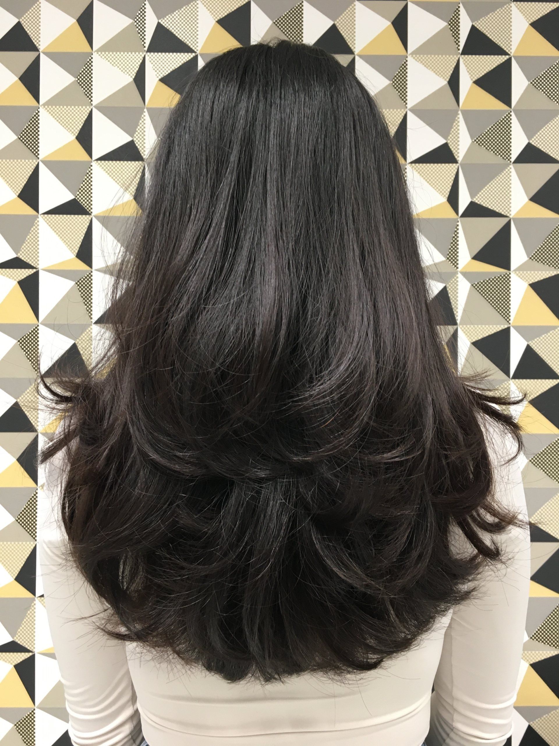 Frau mit langen braunen Haaren vor einer gemusterten Wand