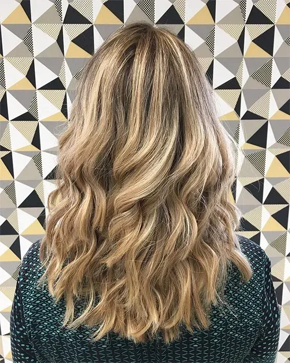 Frau mit welligen blonden Haaren vor einer gemusterten Wand