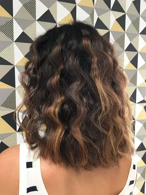 Frau mit welligen braunen Haaren vor einer gemusterten Wand