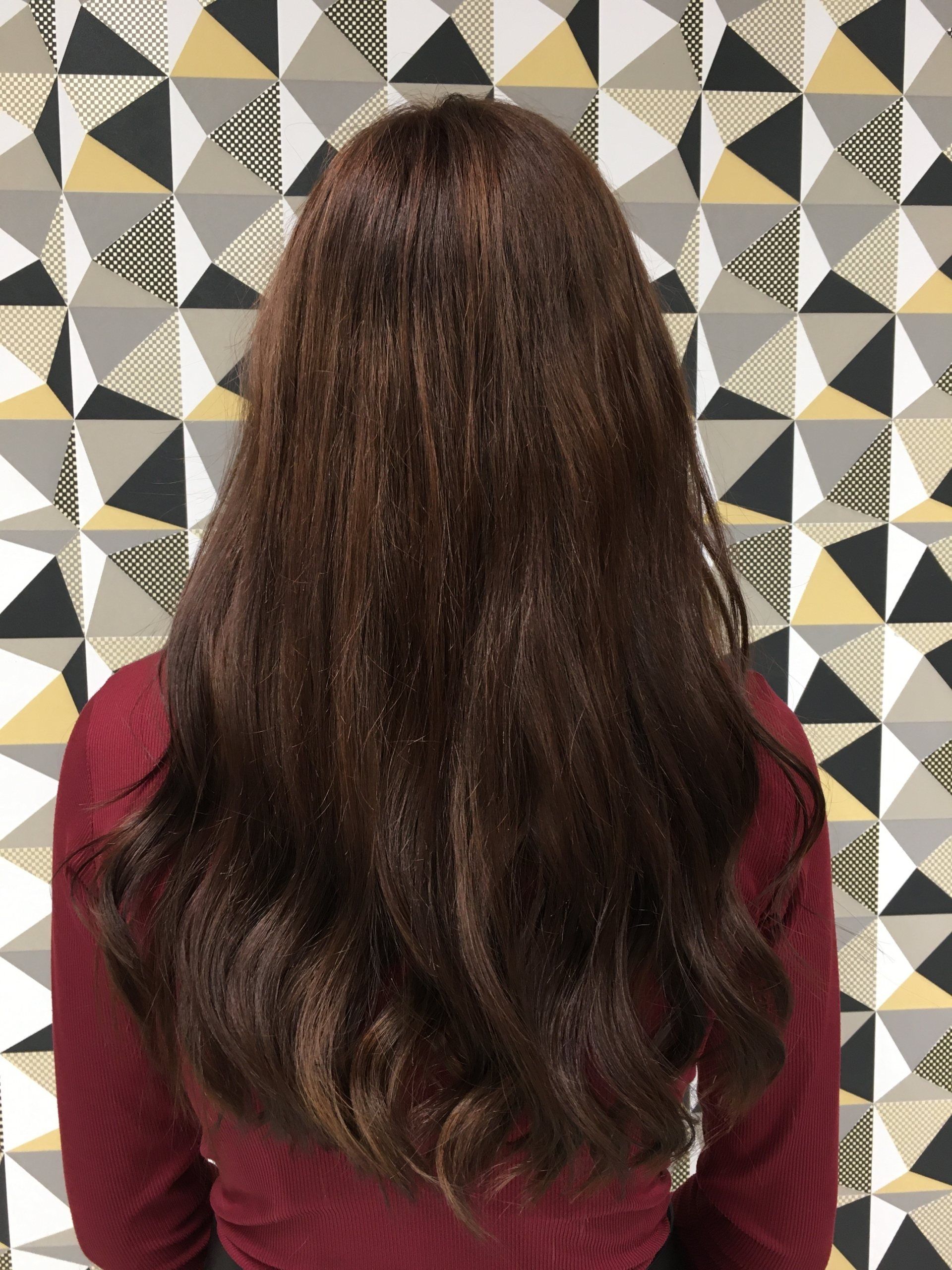 Frau mit langen braunen Haaren vor einer gemusterten Wand