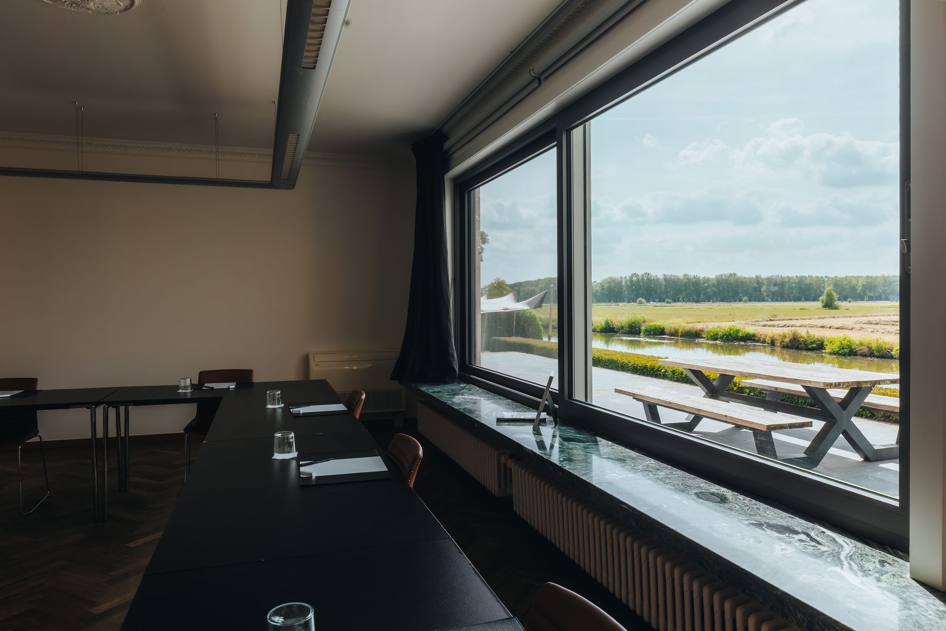 Vergaderruimte met een houten tafel, waterflessen, documenten, stoelen en een flipchart.