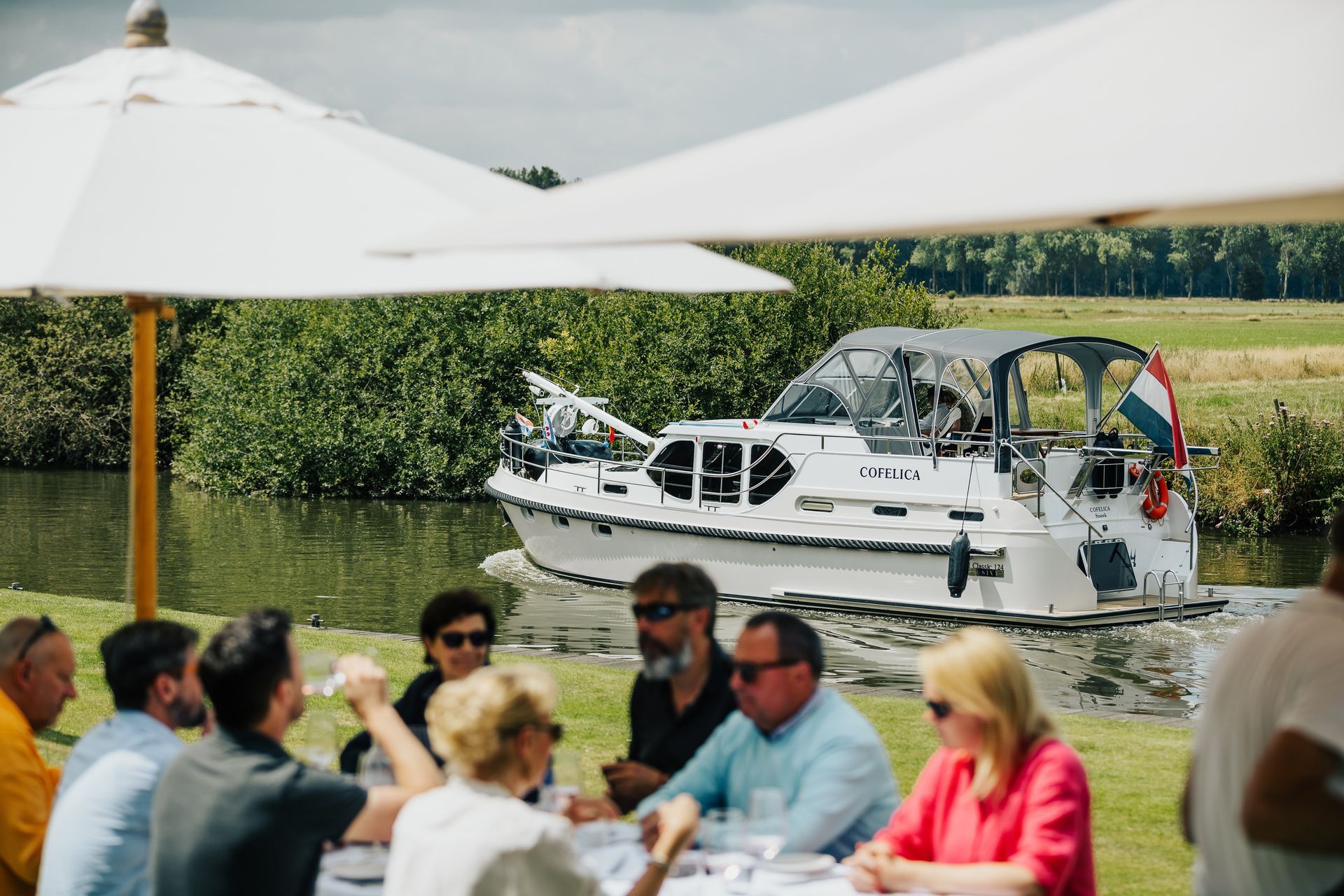 A restaurant with tables , chairs , umbrellas and a lake in the background.