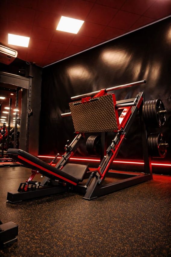 En un gimnasio con poca luz, suelo texturizado e iluminación ambiental, hay una máquina de prensa de piernas