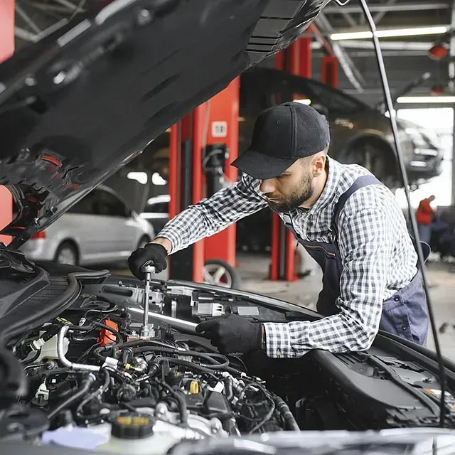 Un hombre está trabajando en el motor de un coche en un garaje.