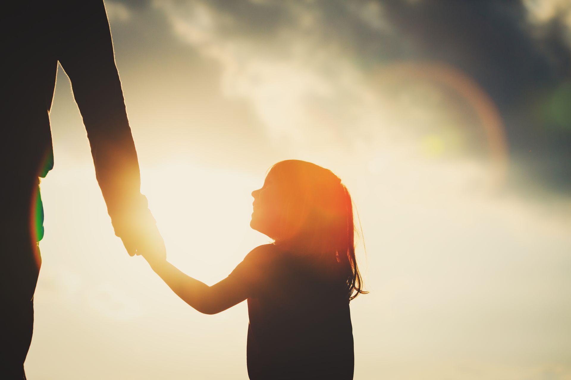 Petite fille tenant la main d'un adulte en contrejour