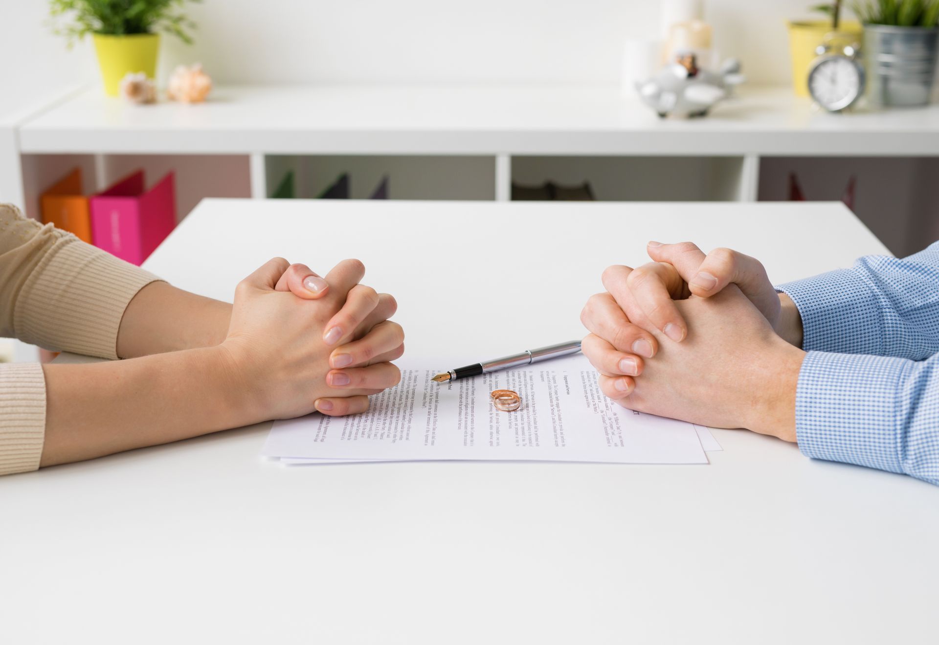 Deux personnes se tiennent la main par-dessus une table lors d'une réunion, un stylo et des papiers entre elles.