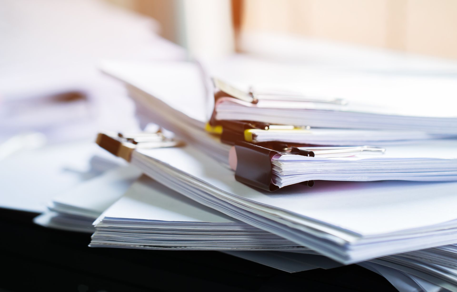 Des piles de feuilles blanches et de dossiers sur un bureau, avec des documents agrafés au premier plan.