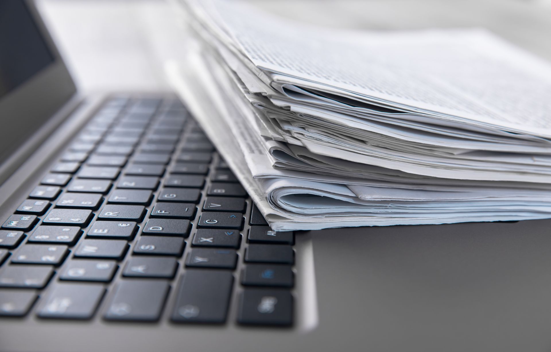 Clavier d'ordinateur portable à côté d'une épaisse pile de documents papier, suggérant un contraste entre travail numérique et travail papier.