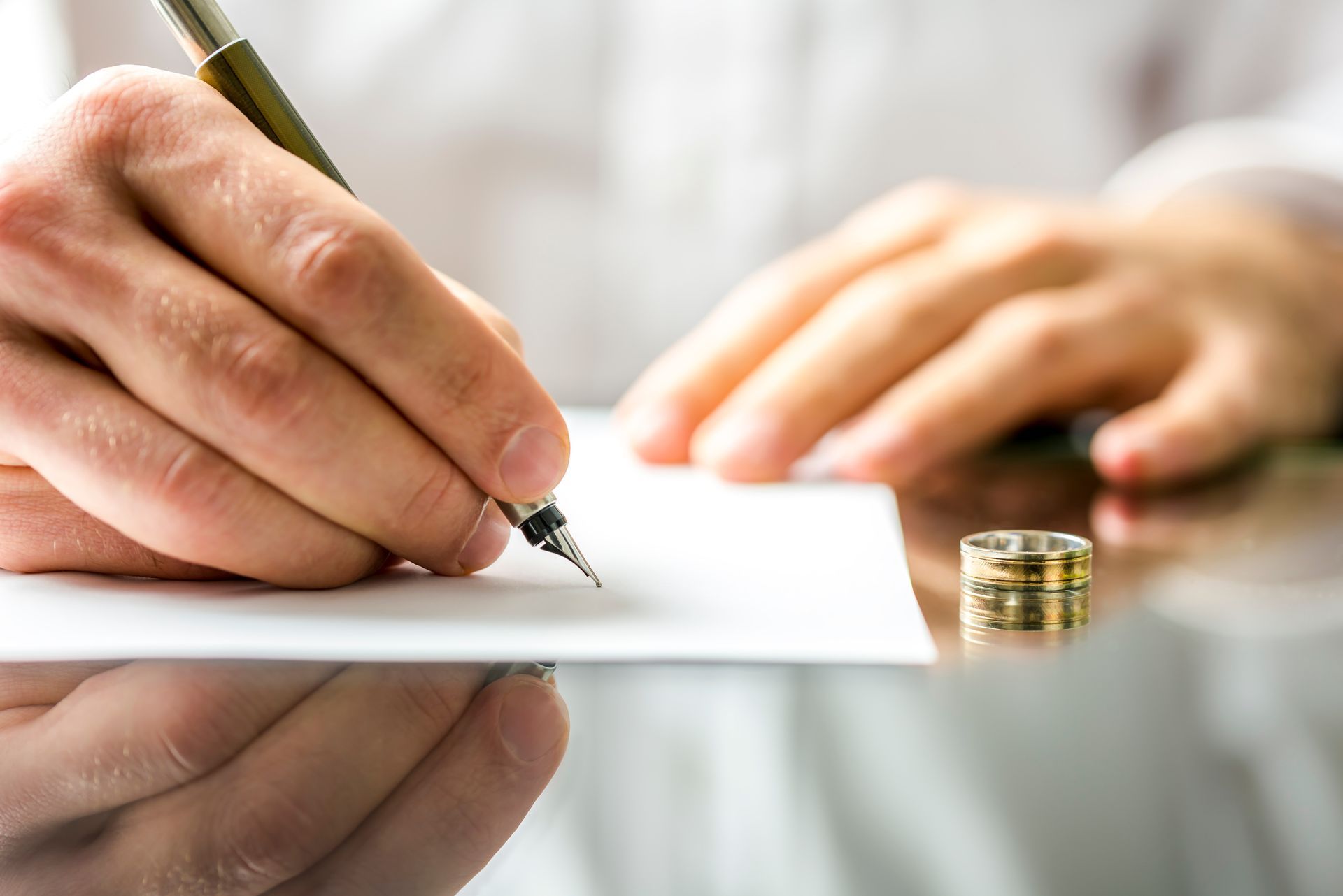 Une main signant un document à côté d'une alliance sur un bureau