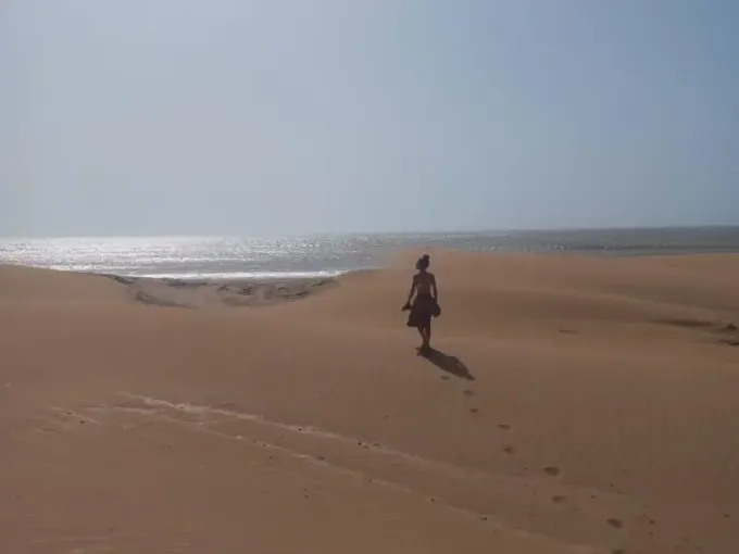 Una persona camina sola a través de una vasta duna de arena dorada hacia el horizonte donde el mar se encuentra