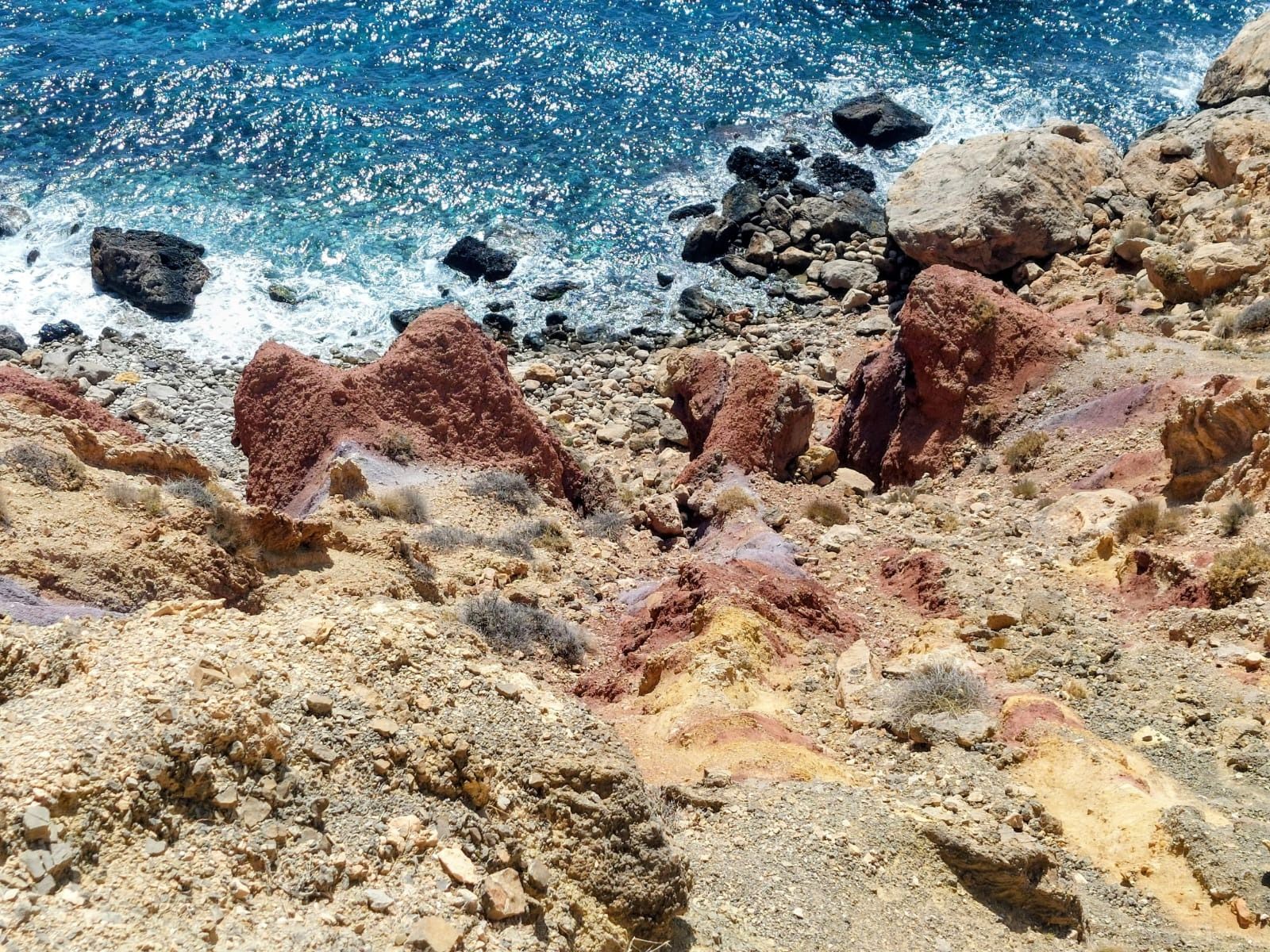 Una vista aérea de una costa rocosa y multicolor con acantilados rojos y tostados que descienden