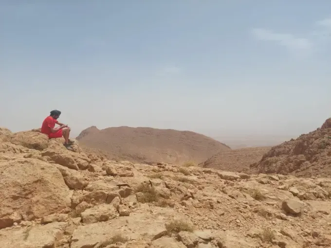 Una persona con una camisa roja está sentada en una cornisa rocosa del desierto, contemplando