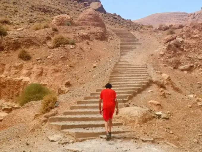 Una persona con una camisa roja sube por una larga escalera de piedra tallada en la ladera rocosa