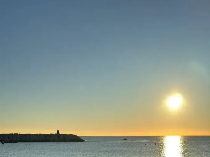Una escena marina iluminada por el sol durante la hora dorada, con un rompeolas rocoso a la izquierda