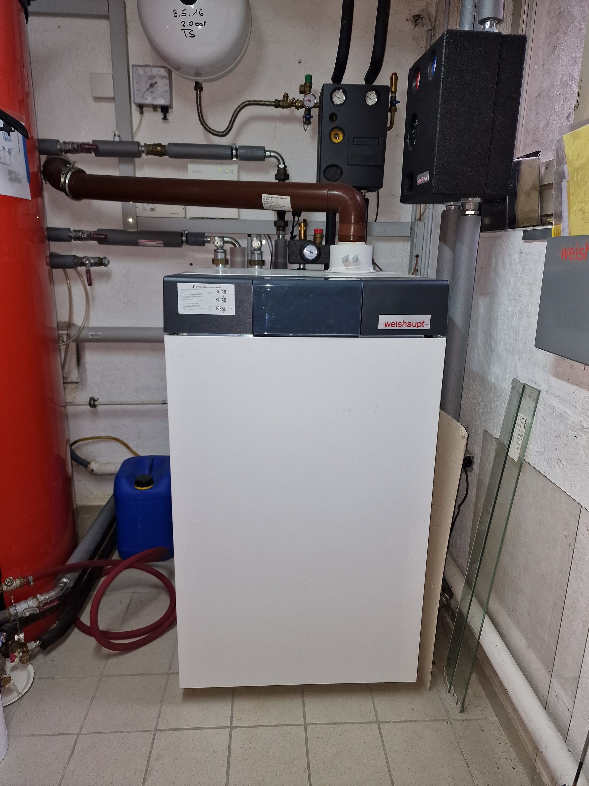 Technikraum mit Rohren, Tanks und Geräten; neutrale Farben.