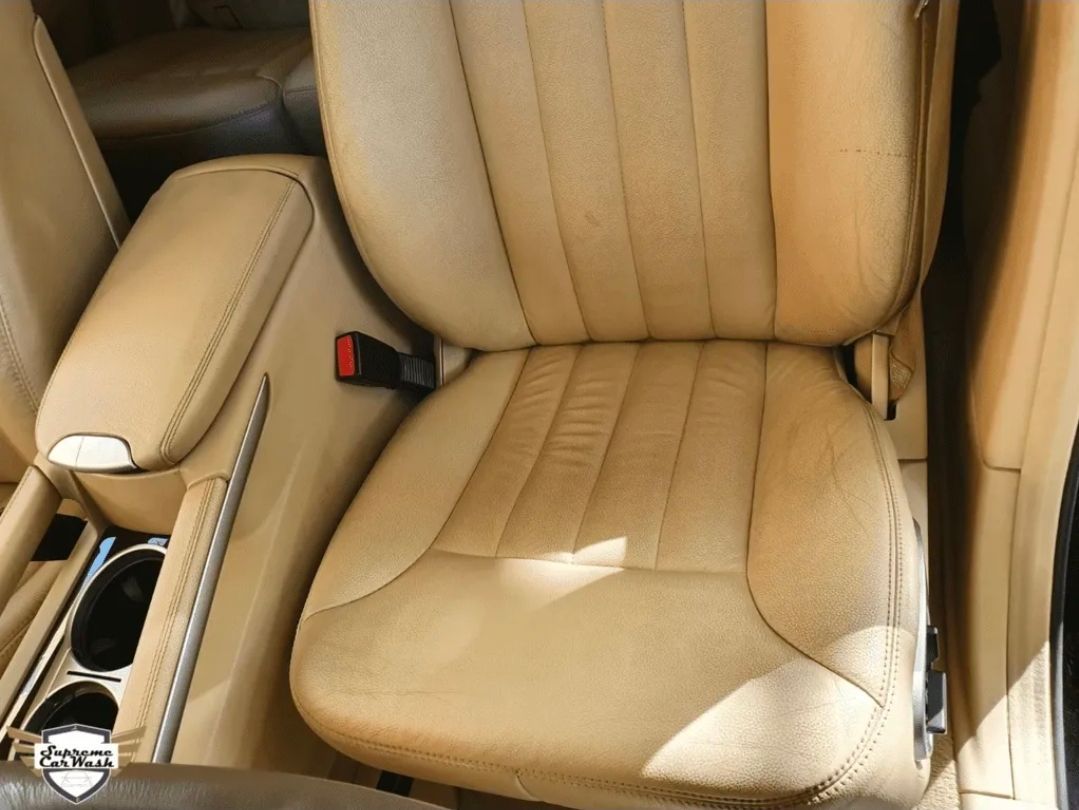 Asiento de coche de cuero beige con costuras verticales y consola central con portavasos.