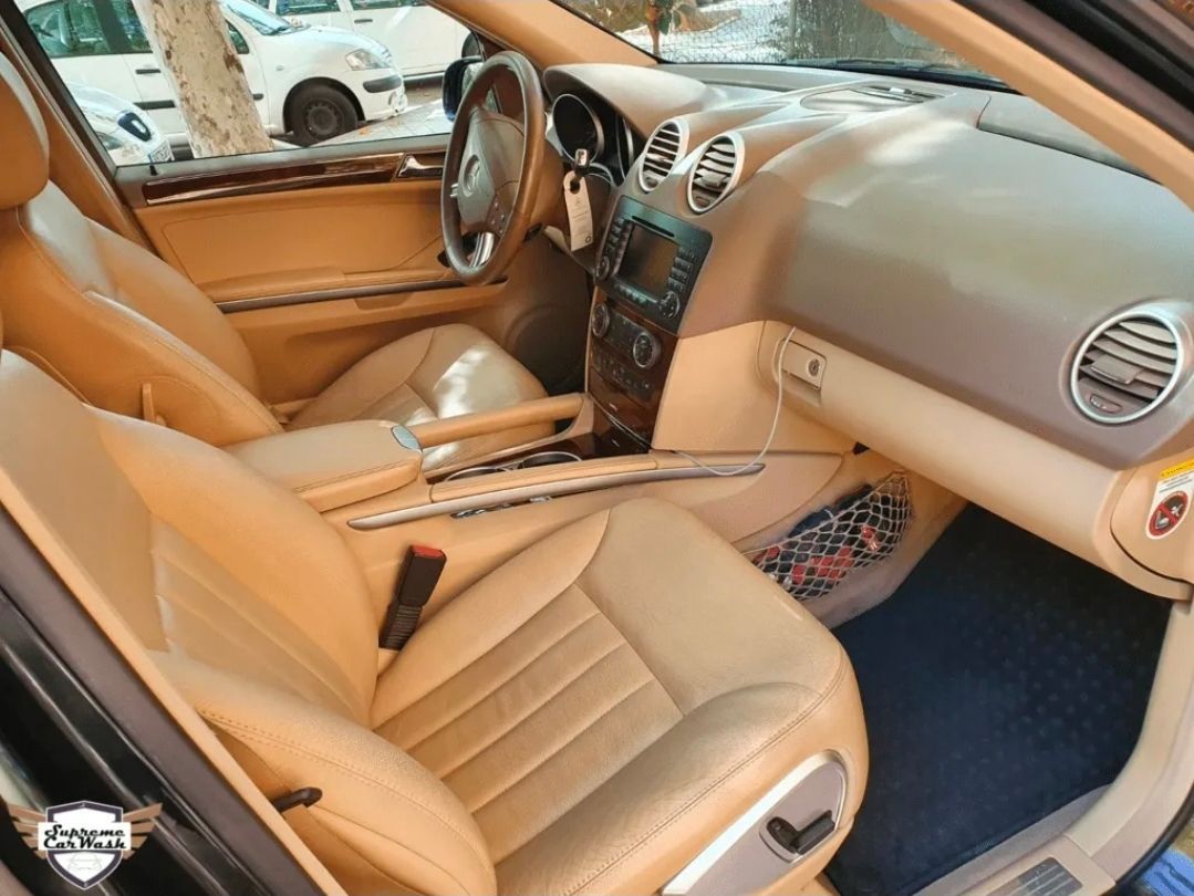 Interior del coche en cuero color canela con detalles de madera en el salpicadero, el volante y las alfombrillas oscuras.