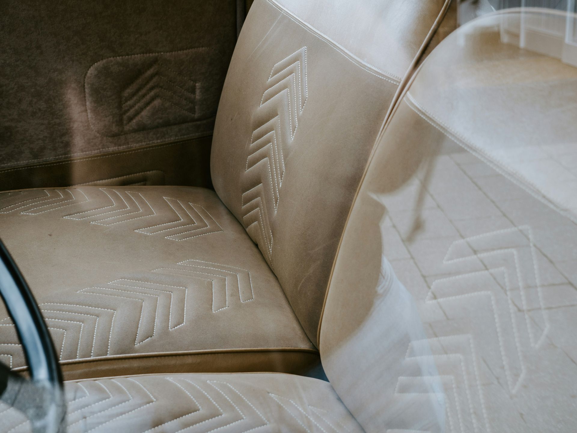 Asientos de coche de color beige con un patrón de costura en zigzag o espiga que se repite, con una vista parcial del volante.