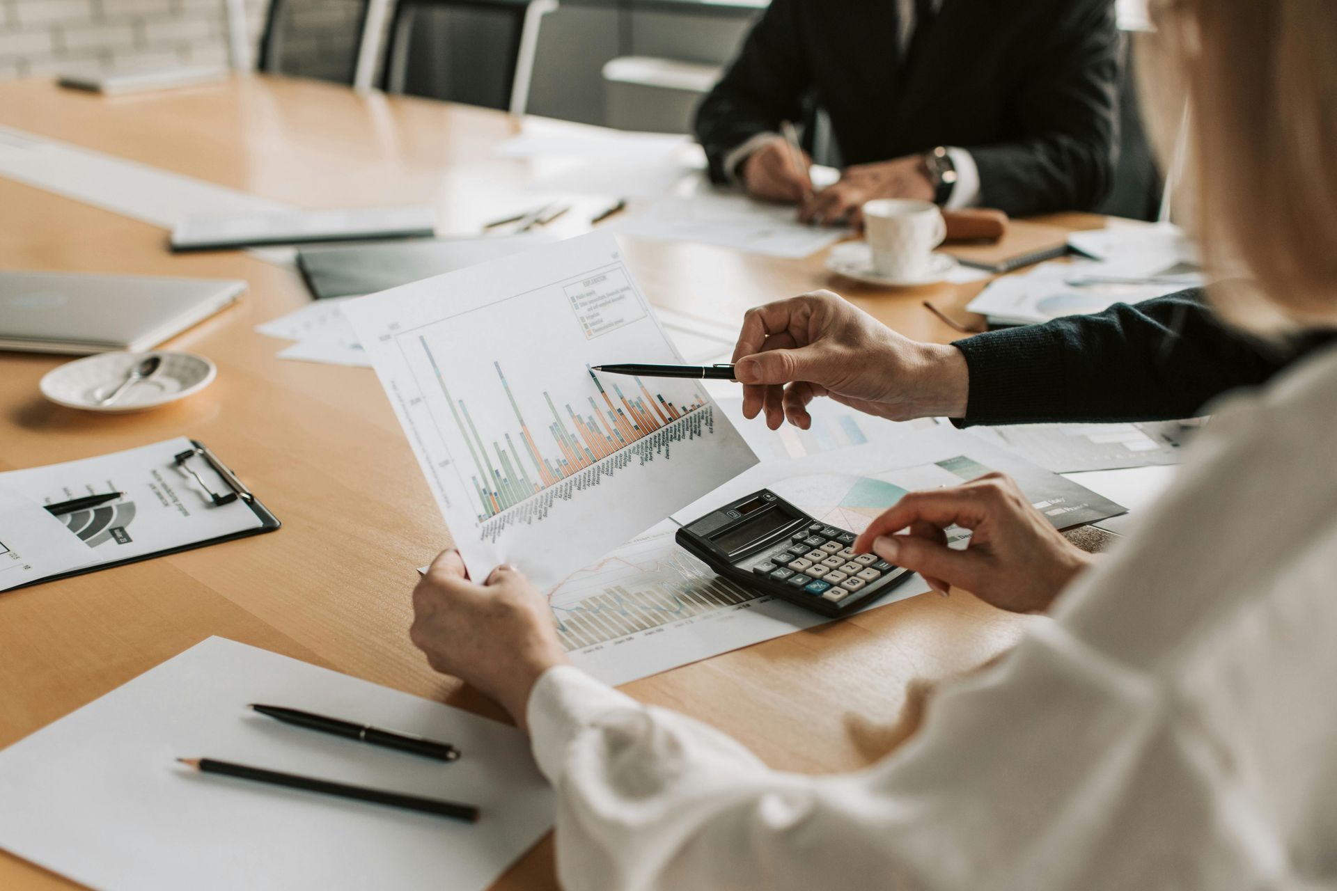 Las personas en una mesa revisan gráficos, usando una calculadora y señalando los datos.