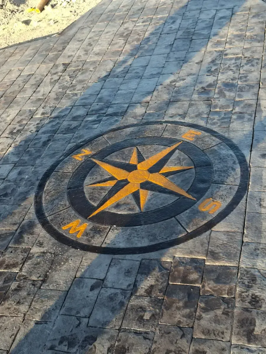 Una incrustación de una rosa de los vientos dorada se encuentra en el centro de un patio de adoquines de piedra texturizada de color gris oscuro.