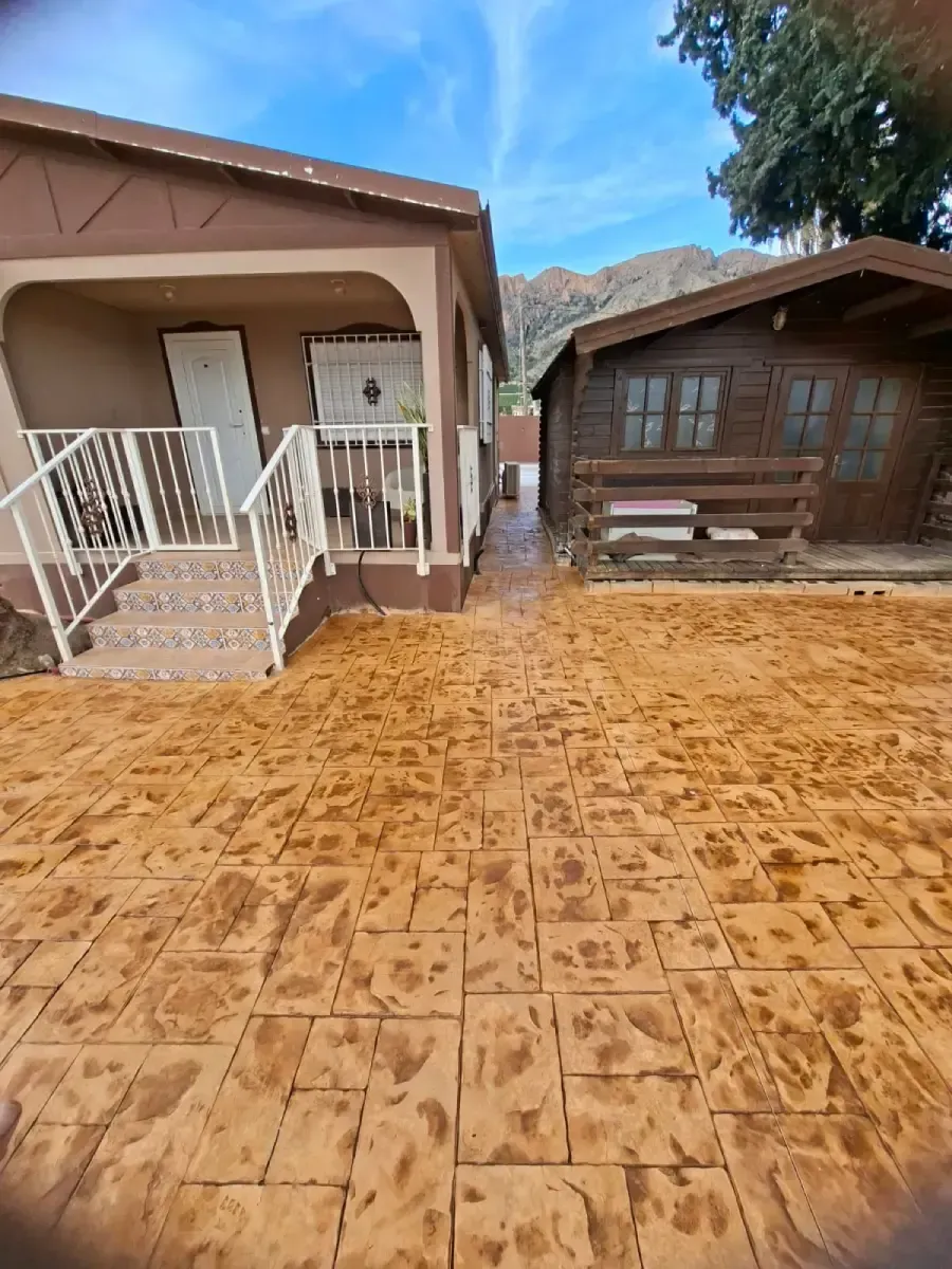 Entrada de cemento gris que conduce a una puerta metálica. Detrás de la puerta hay un edificio y algunos árboles.
