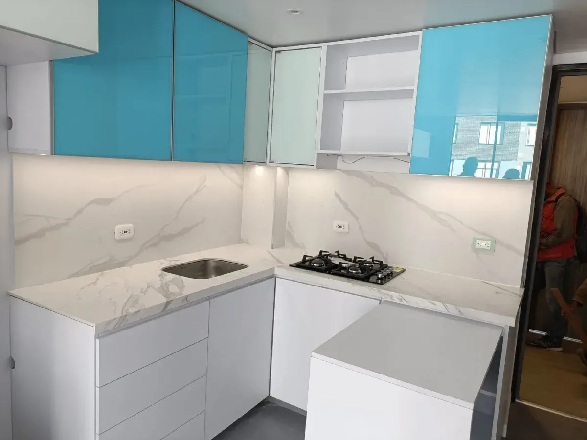 Cocina moderna con gabinetes blancos y azules, salpicadero de mármol y estufa a gas.