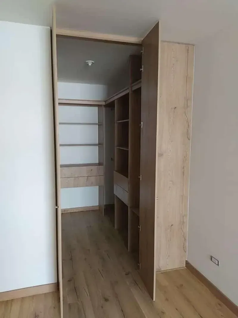 Armario abierto de madera en una habitación con suelos de madera clara y paredes blancas.