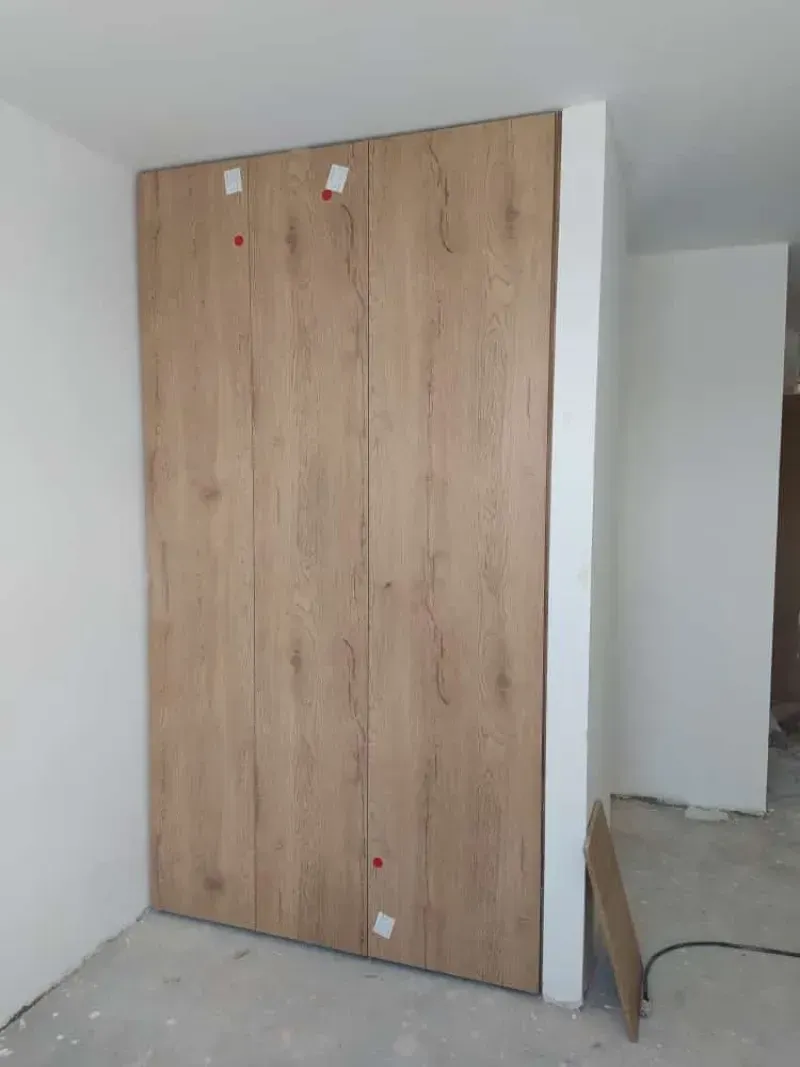 Puertas de armario de madera instaladas en un rincón de una habitación, con paredes blancas y piso de concreto.