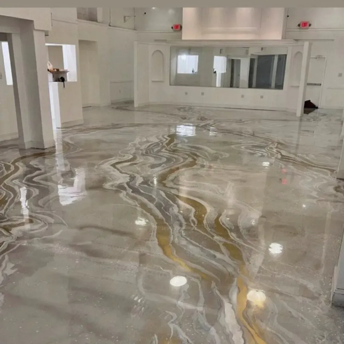 Piso epoxi brillante con efecto mármol, con remolinos dorados y plateados en una habitación vacía de paredes blancas.