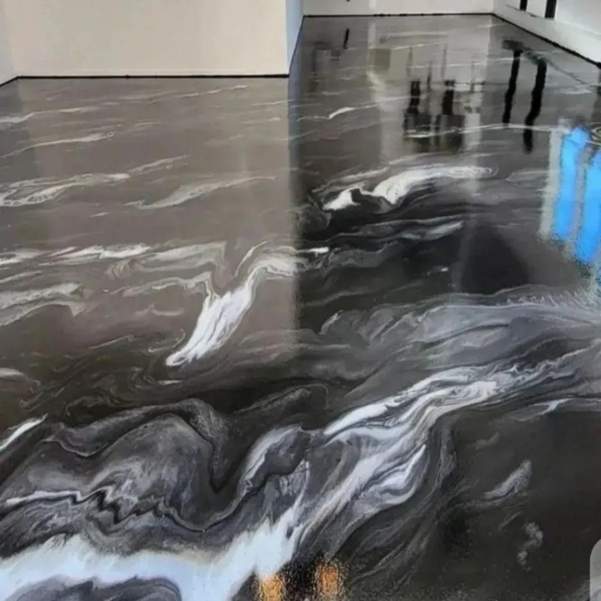 Suelo de epoxy en tonos negros, blancos y grises con efecto remolino en una estancia, con acabado brillante y reflejos.
