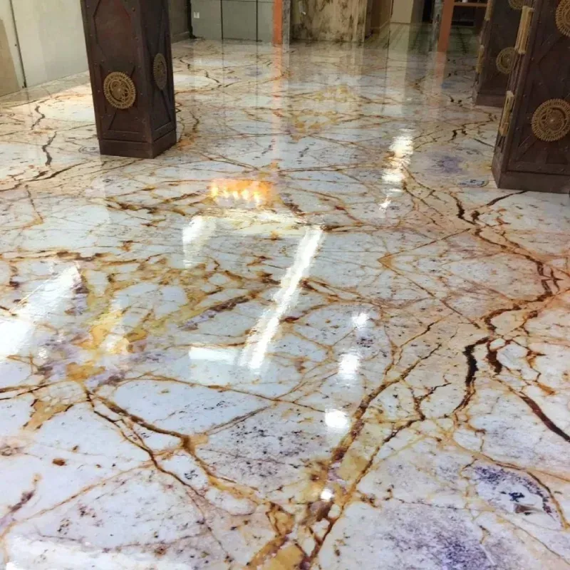 Suelo de mármol pulido con vetas doradas y marrones que reflejan la luz. Pilares al fondo.