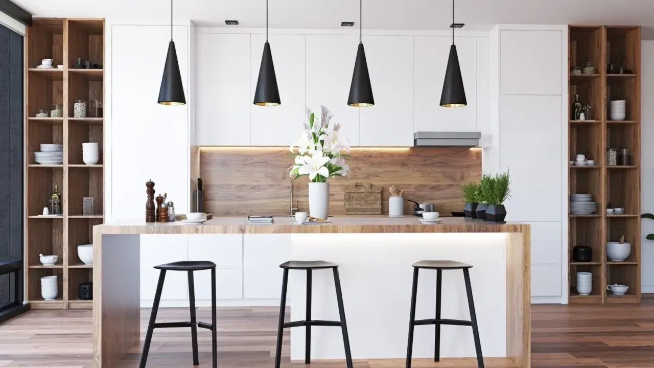 Cocina moderna con gabinetes blancos, detalles de madera, luces colgantes negras e isla con taburetes.