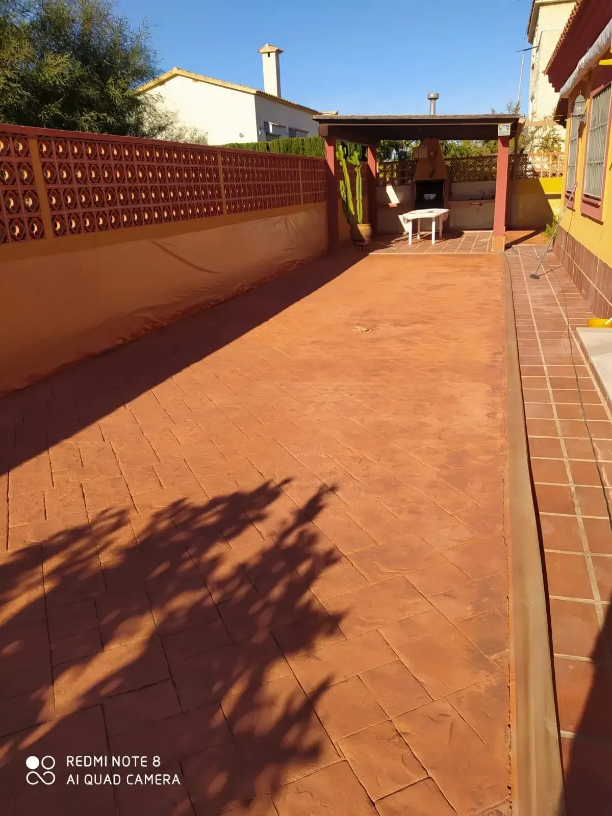 Patio largo pavimentado con ladrillo, con zona de barbacoa incorporada bajo una pérgola de madera