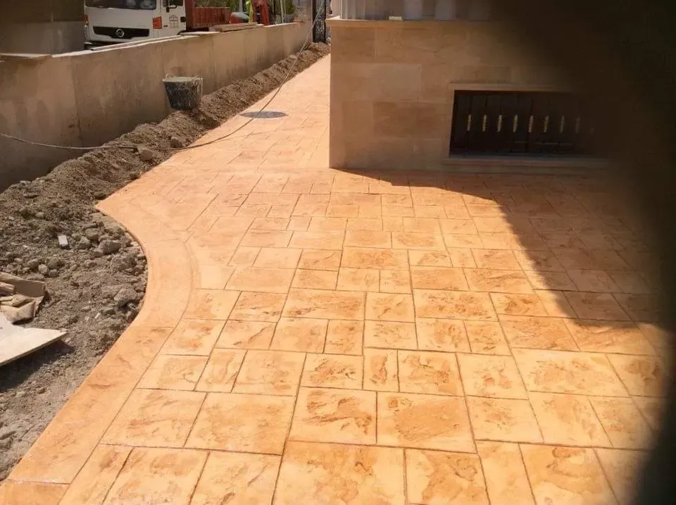 Un patio exterior de hormigón con barbacoa de obra y un seto de vegetación al fondo.