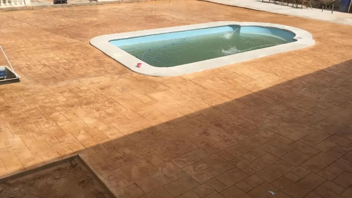 Piscina con patio de hormigón estampado marrón.