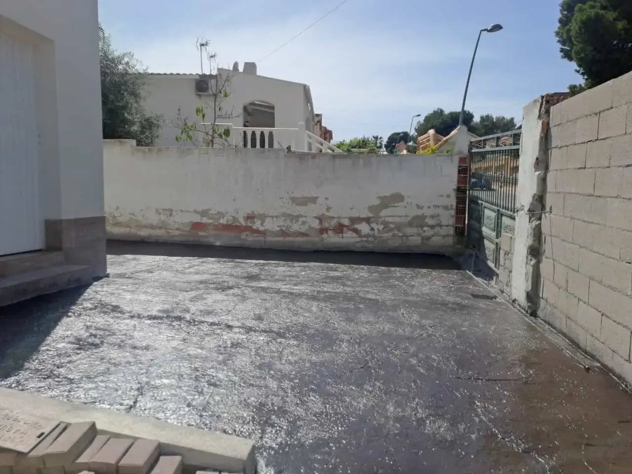 Un área húmeda y pavimentada de color gris oscuro entre paredes blancas y una pared de ladrillo con una puerta