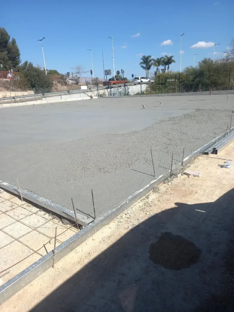 Losa de hormigón recién vertida en una obra en construcción, con estructura metálica y refuerzo visibles.