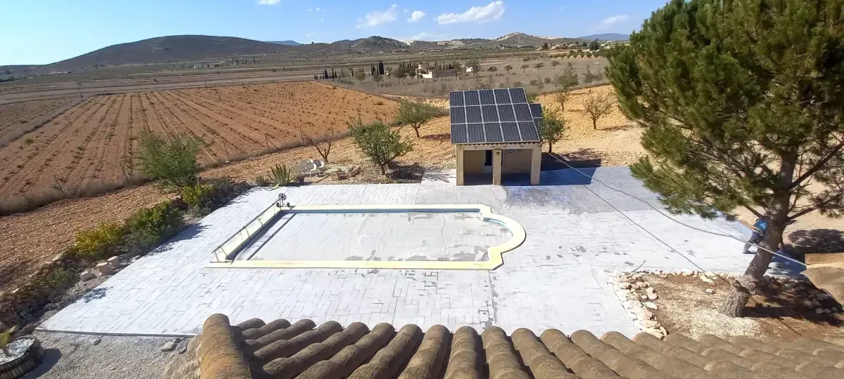 Vista aérea de un área de piscina con un pequeño edificio, rodeado de tierras de cultivo y montañas.