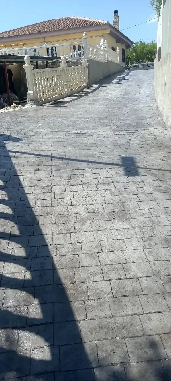 Una calle inclinada y pavimentada con ladrillos se curva junto a una casa amarilla con techo de tejas y una pared decorativa